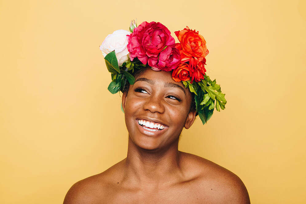 Ozontherapie Hamburg - Zahnfleischbeschwerden - Eine junge Frau mit Blumen auf dem Kopf lächelt unbeschwert, da Sie keine Zahnfleischbeschwerden mehr hat
